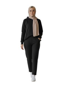 Person wearing a black outfit with a beige hijab on a plain background